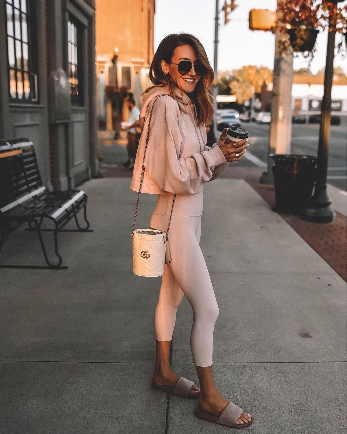 @karinastylediaries wearing a light pink capri legging with matched cropped sweatshirt with slides, a designer purse, and sunglasses while grabbing a coffee.