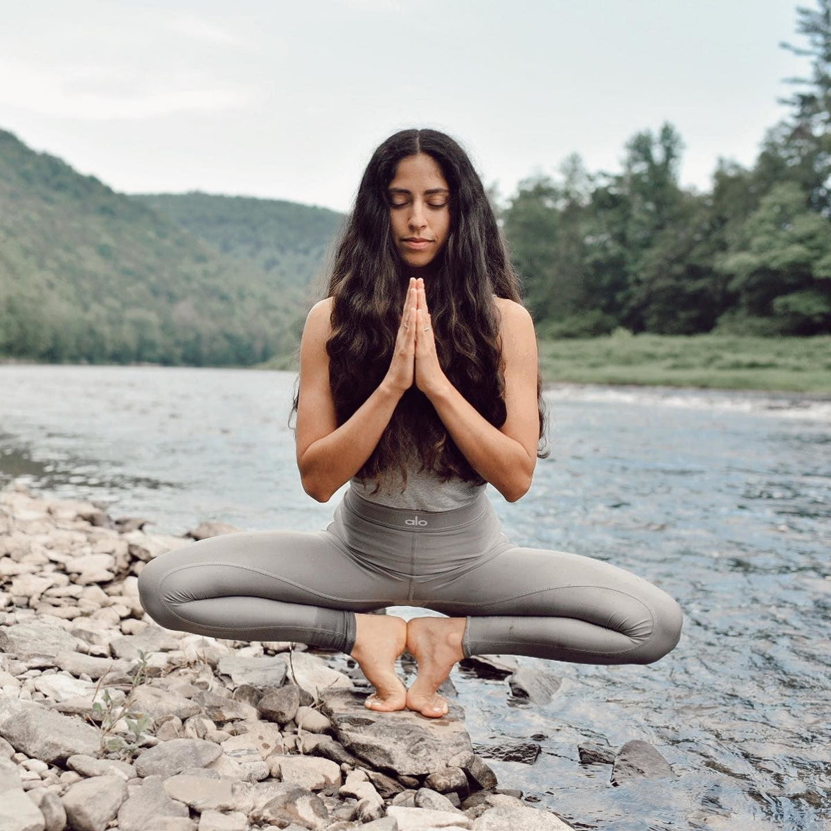 @lamise wearing high-waisted yoga leggings while meditating alongside a flowing river in the mountains.